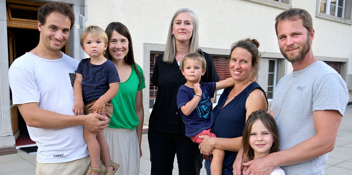 Un groupe de sept personnes, dont quatre adultes et trois enfants, pose ensemble devant un bâtiment beige avec des fenêtres.