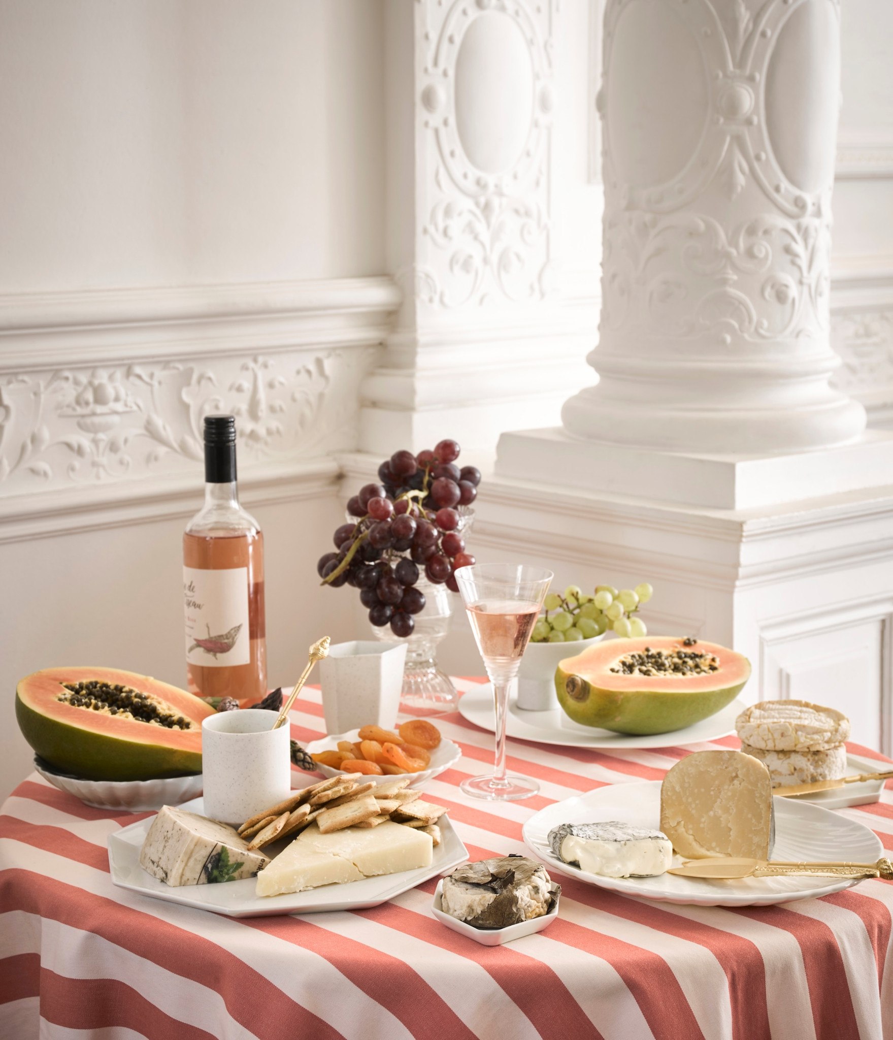 Gedeckter Tisch in Antwerpen mit Käse, Papaya, Trauben, Crackern und Roséwein vor weisser Stuckverzierung.