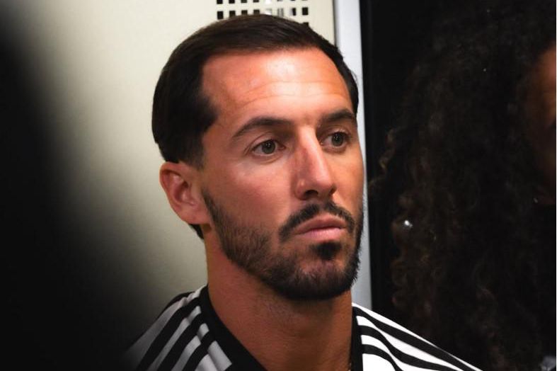 Un homme portant une chemise rayée, avec une expression sérieuse, regarde droit devant lui.