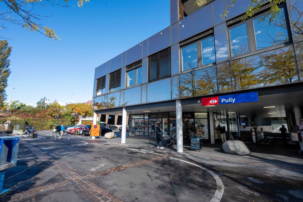 Gare CFF de Pully sous un ciel bleu, avec des arbres d'automne et des passants. Photo prise par Patrick Martin.