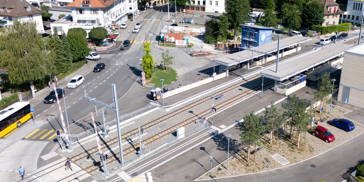 Luftaufnahme des Bahnhofareals Nidau, mit mehreren Autos und Häusern im Hintergrund.