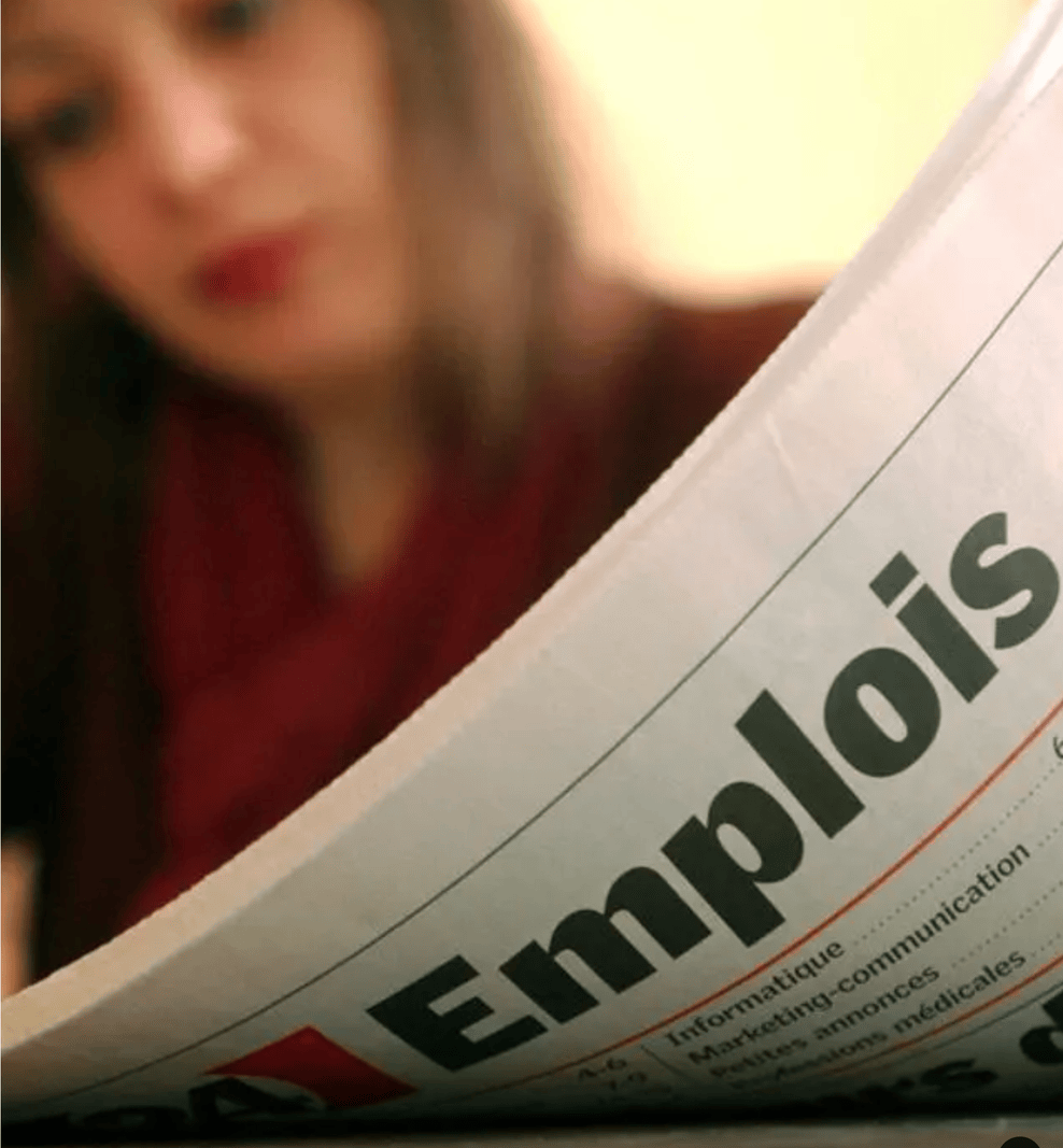 Gros plan sur un journal ouvert avec le mot 'Emplois' en gros titre, en arrière-plan une silhouette floue.