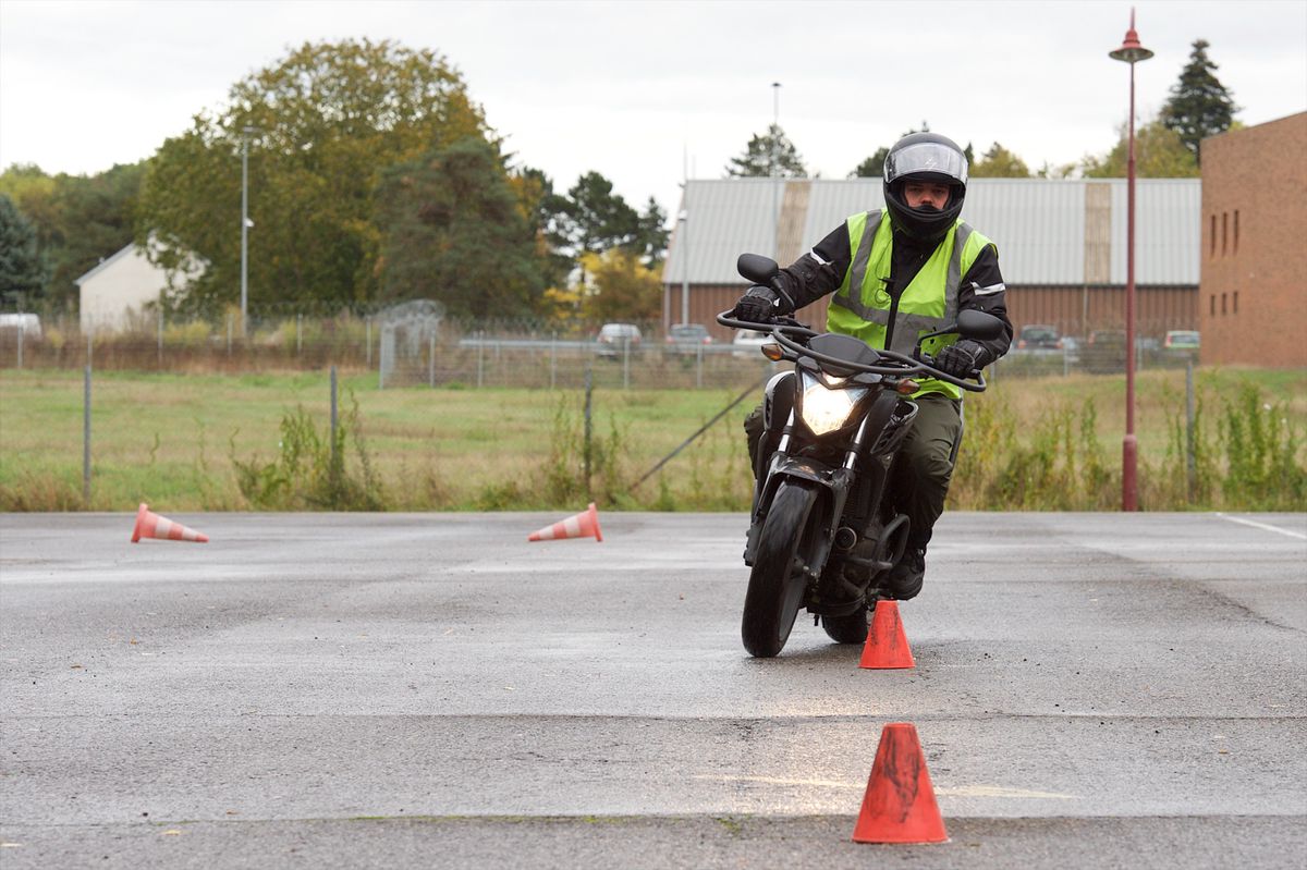 Un élève en gilet de sécurité vert pratique la conduite à moto autour de cônes en extérieur à Luxembourg-Findel.