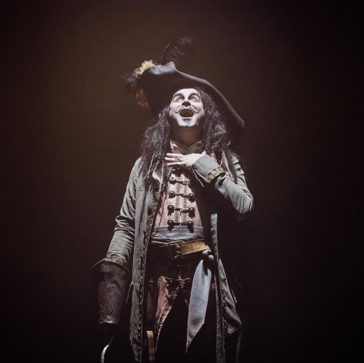 Personnage déguisé en pirate sur scène, portant un tricorne et une veste longue, éclairé par une lumière théâtrale.