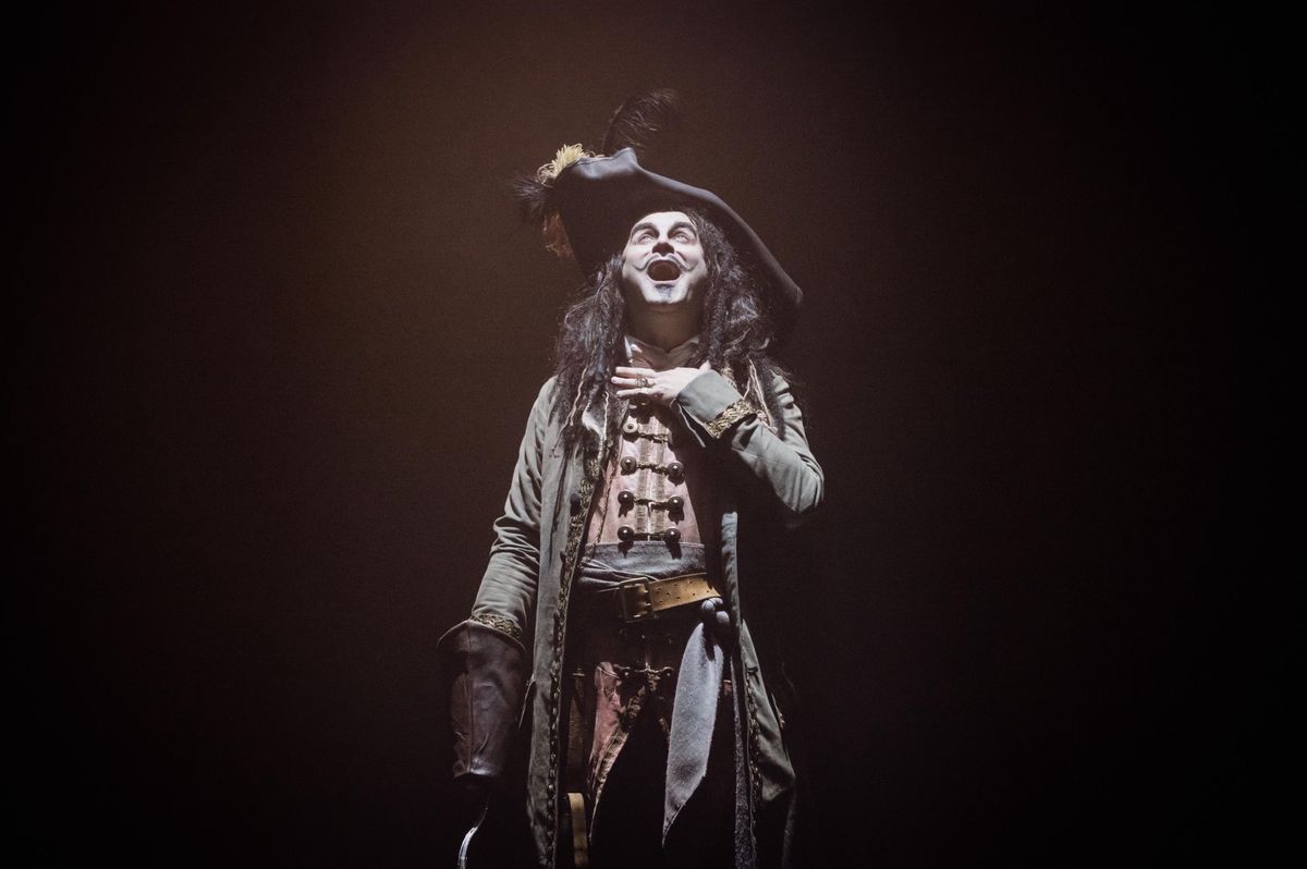 Personnage déguisé en pirate sur scène, portant un tricorne et une veste longue, éclairé par une lumière théâtrale.