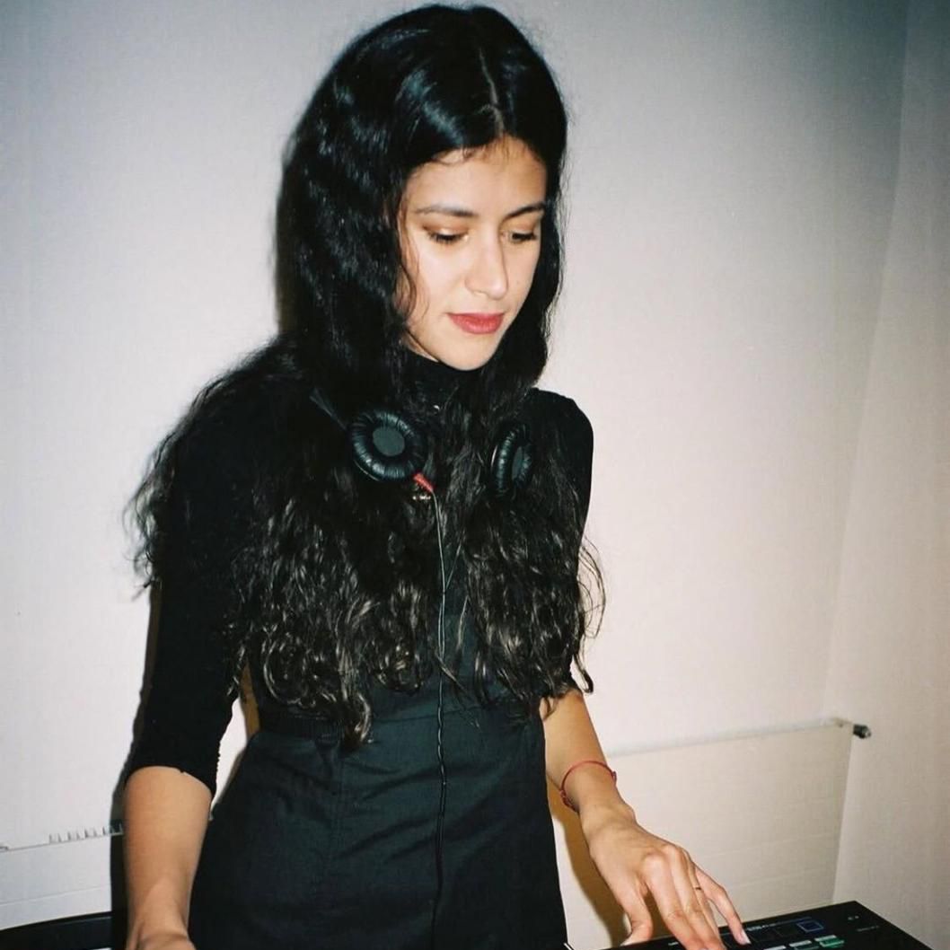 Eine Frau mit langen dunklen Haaren steht an einem DJ-Pult und konzentriert sich auf das Mischen von Musik.