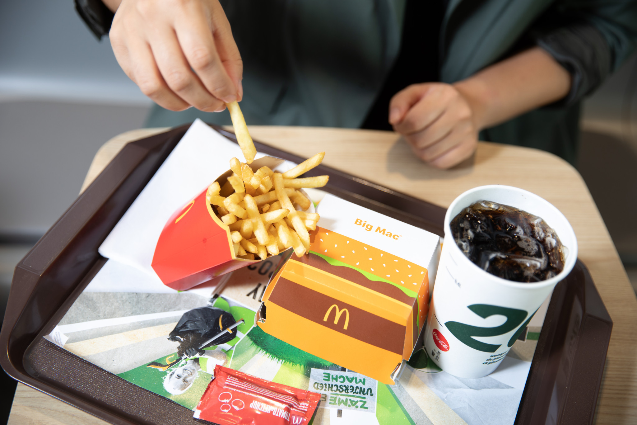 Person nimmt Pommes frites aus einer McDonald’s-Packung auf einem Tablett mit Burger, Getränk und Ketchup an einem Tisch in Zürich.