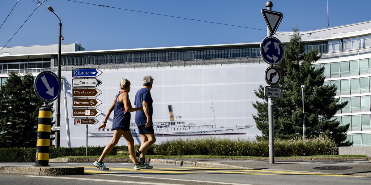Deux personnes passent devant une grande photographie intitulée 'Belle époque' du bateau à vapeur 'La Suisse', accrochée sur la façade du siège de Nestlé à Vevey par des ouvriers, dans le cadre de la 9e biennale des arts visuels 'Images Vevey', le 24 août 2024.