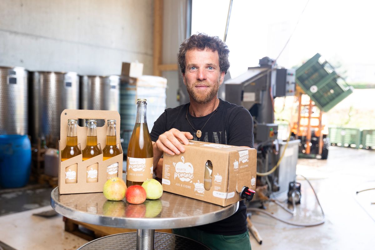 Julien Corminboeuf présente des bouteilles et un carton de jus de pommes de la marque Pressoir Pour ta Pomme dans une installation de pressage à Cugy.
