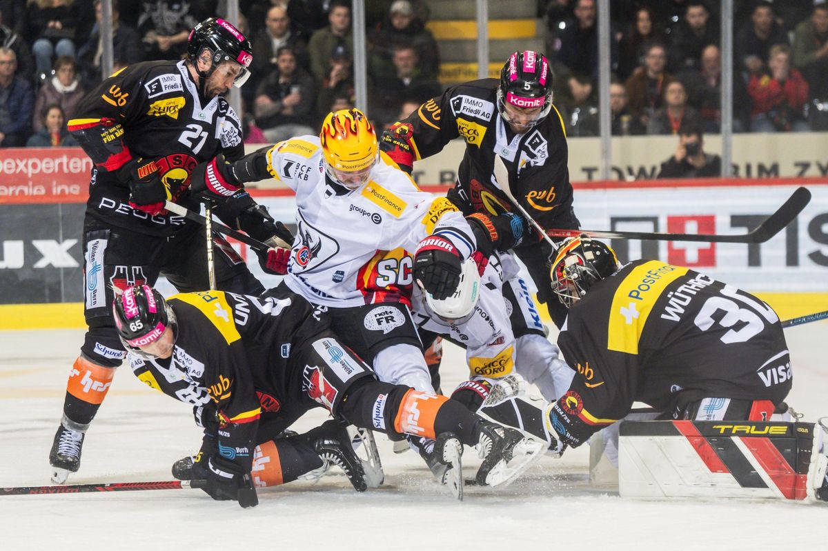 Joueurs de SC Bern et HC Fribourg-Gottéron luttant pour le palet lors du cinquième match de quart de finale des playoffs de la National League, le 22 mars 2025 à la PostFinance Arena à Berne.