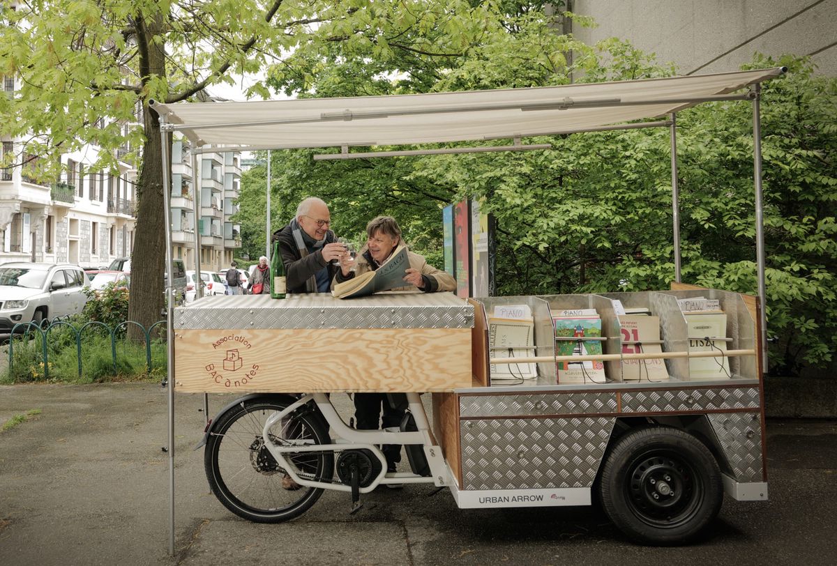 Genève, le 26 avril 2024. Rencontre avec François Creux, créateur d'un vélo-librairie musicale. Avec son deux-roues aménagé pour contenir des partitions, il ira à la rencontre des musiciens dans les écoles de musique, les concerts, les festivals et les brocantes. Ici, en compagnie de Pierre Maulini.