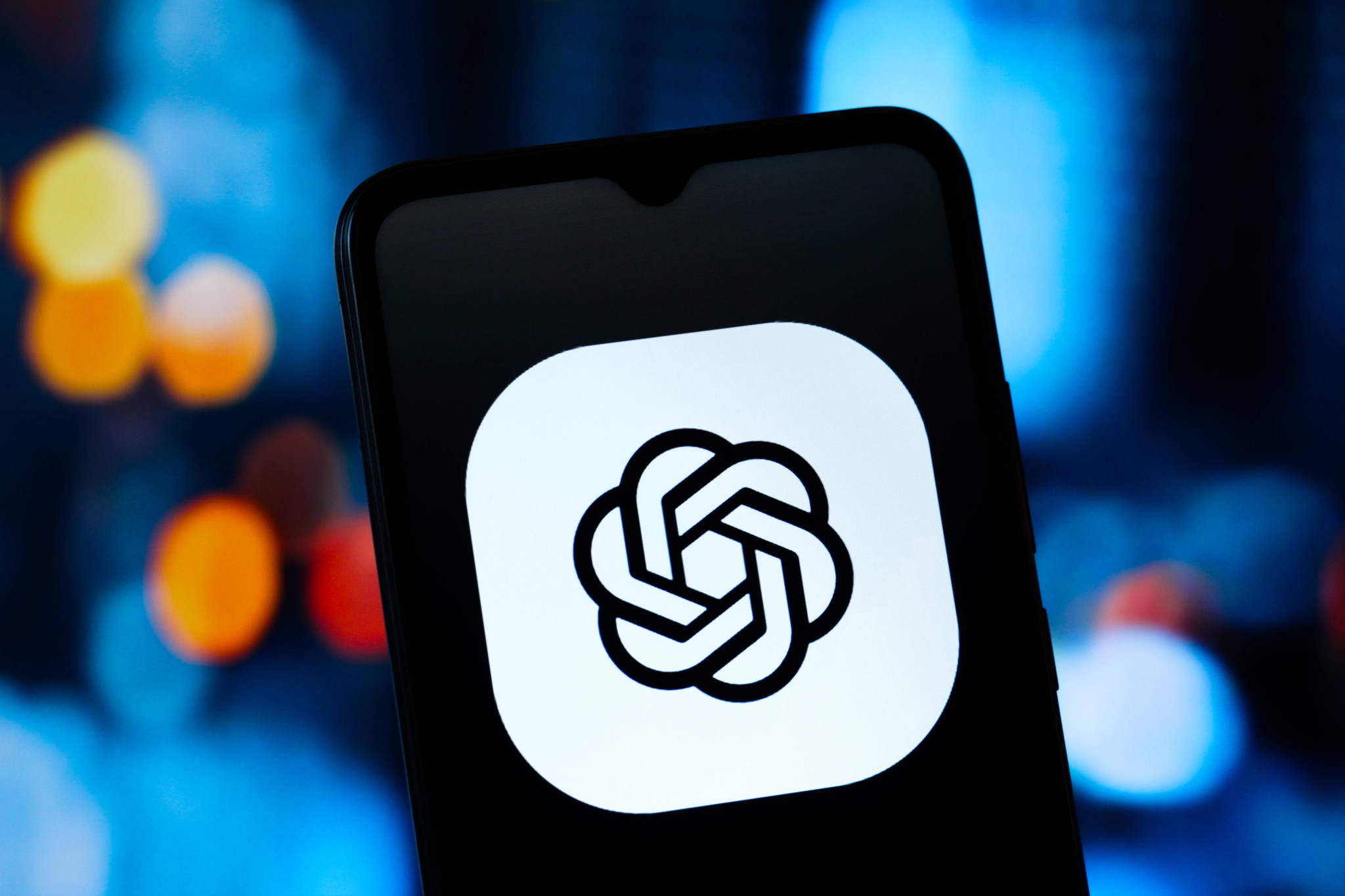 Le logo de ChatGPT d’OpenAI affiché sur l’écran d’un smartphone, sur fond de lumières colorées floues.