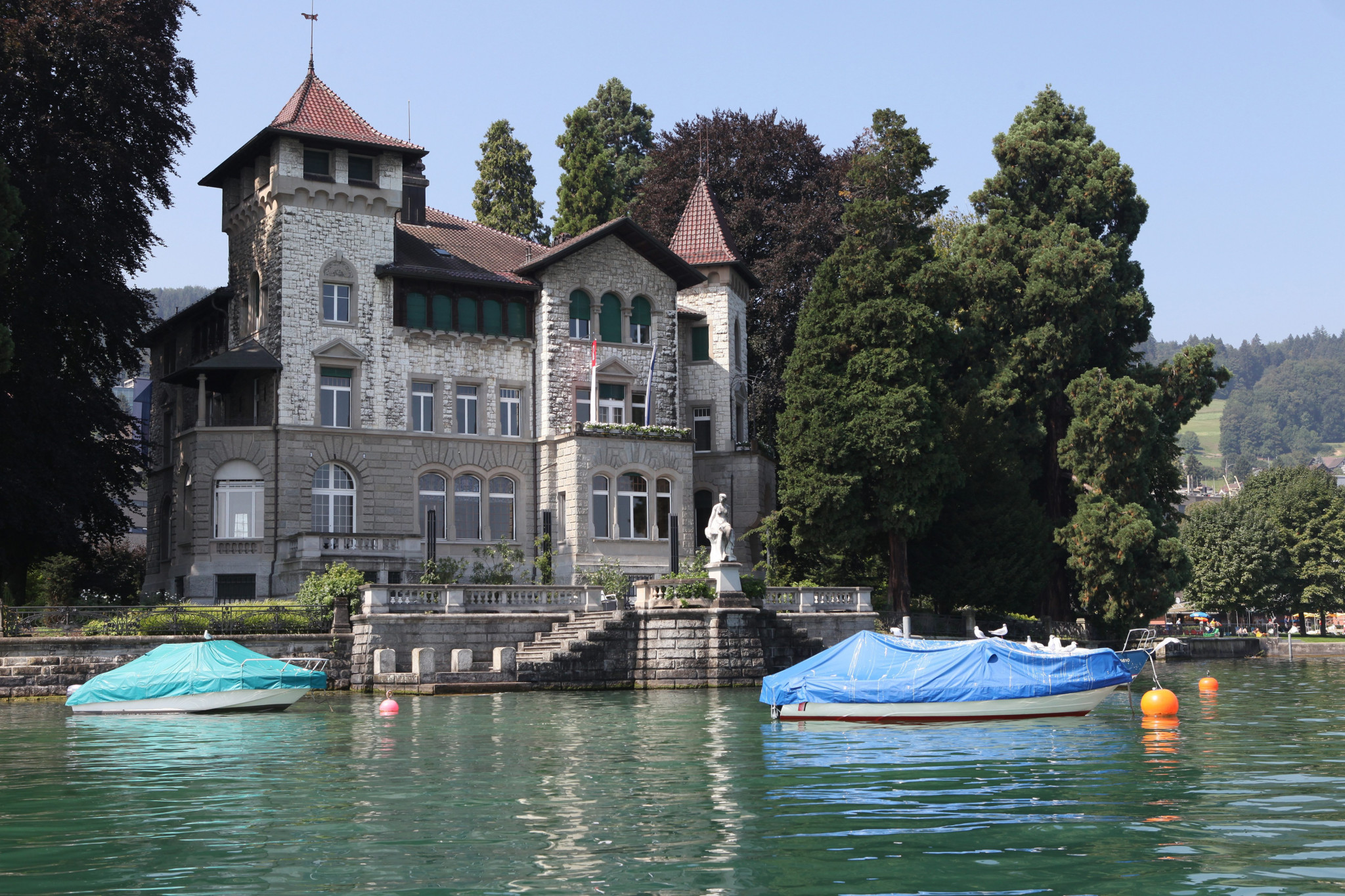 Villa Seerose in Horgen, vom See aus gesehen: Historisches Steingebäude mit Türmchen, Skulptur und Booten am Ufer.