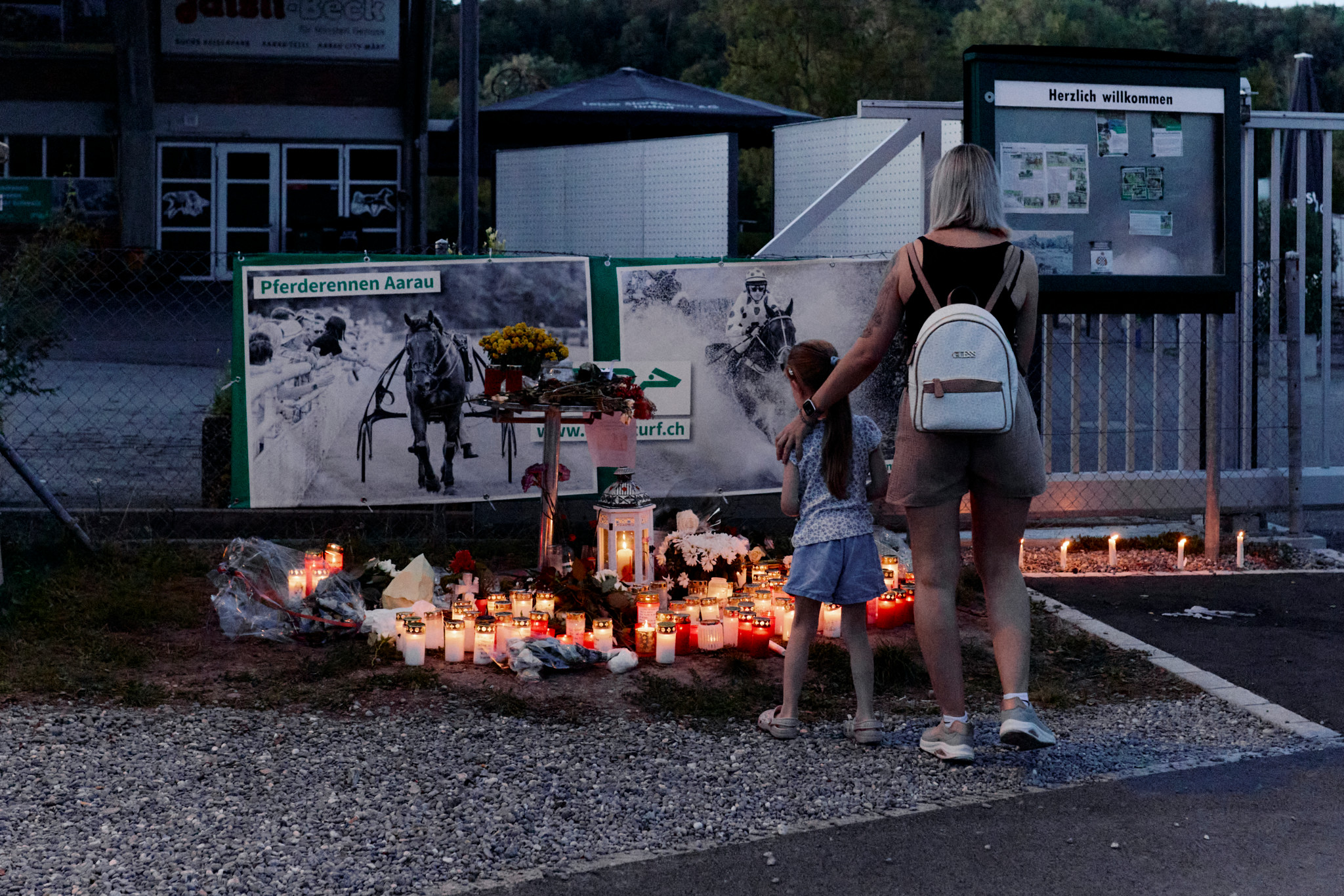 Frau und Kind stehen vor einem Kerzen- und Blumenmeer beim Pferderennen Aarau – Gedenkstätte nach dem Attentat am Rave in Aarau.