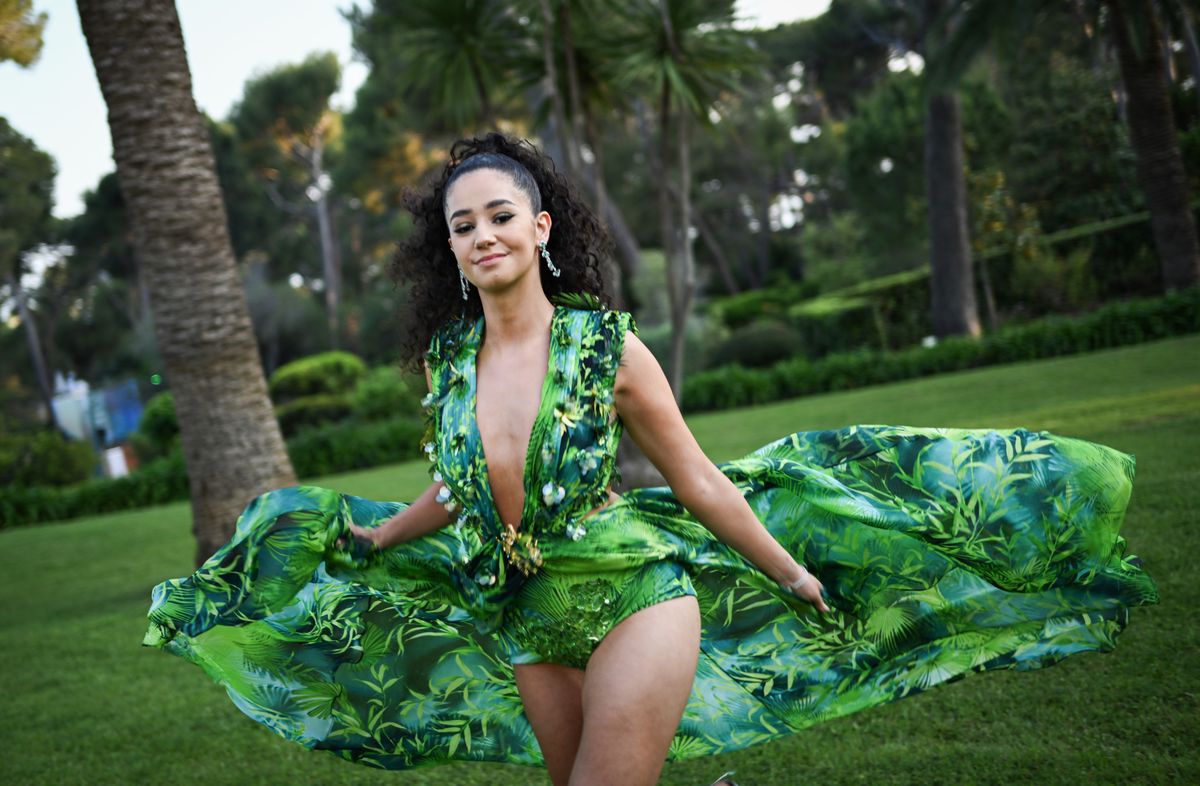 Léna Mahfouf au Gala amfAR Cannes 2023 à l'Hôtel du Cap-Eden-Roc, portant une robe verte avec une traîne fluide, dans un jardin verdoyant.