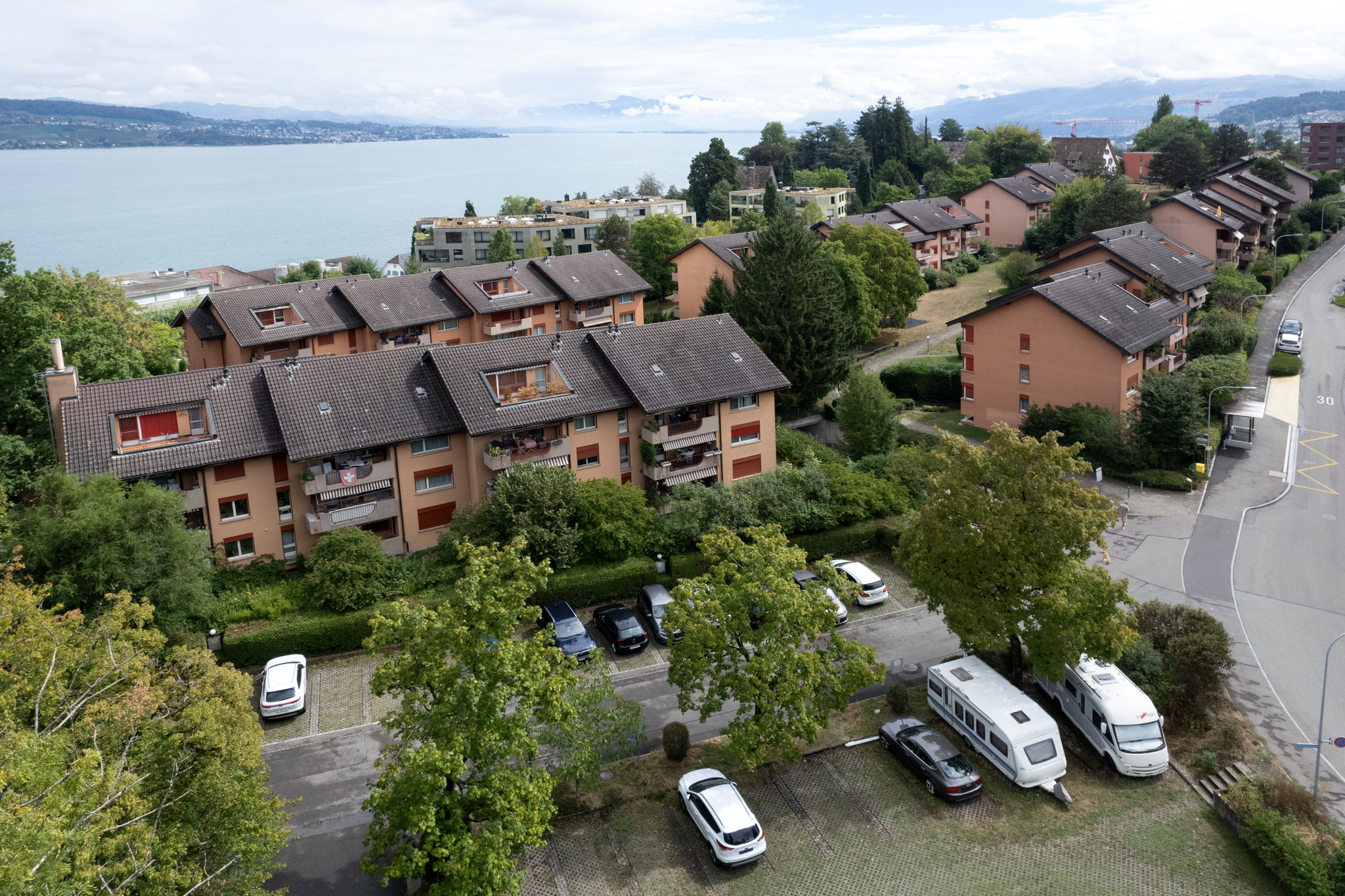 Luftaufnahme der Swiss Life Wohnsiedlung Neudorf in Wädenswil mit mehrstöckigen Mehrfamilienhäusern, Parkplätzen und Zürichsee im Hintergrund.