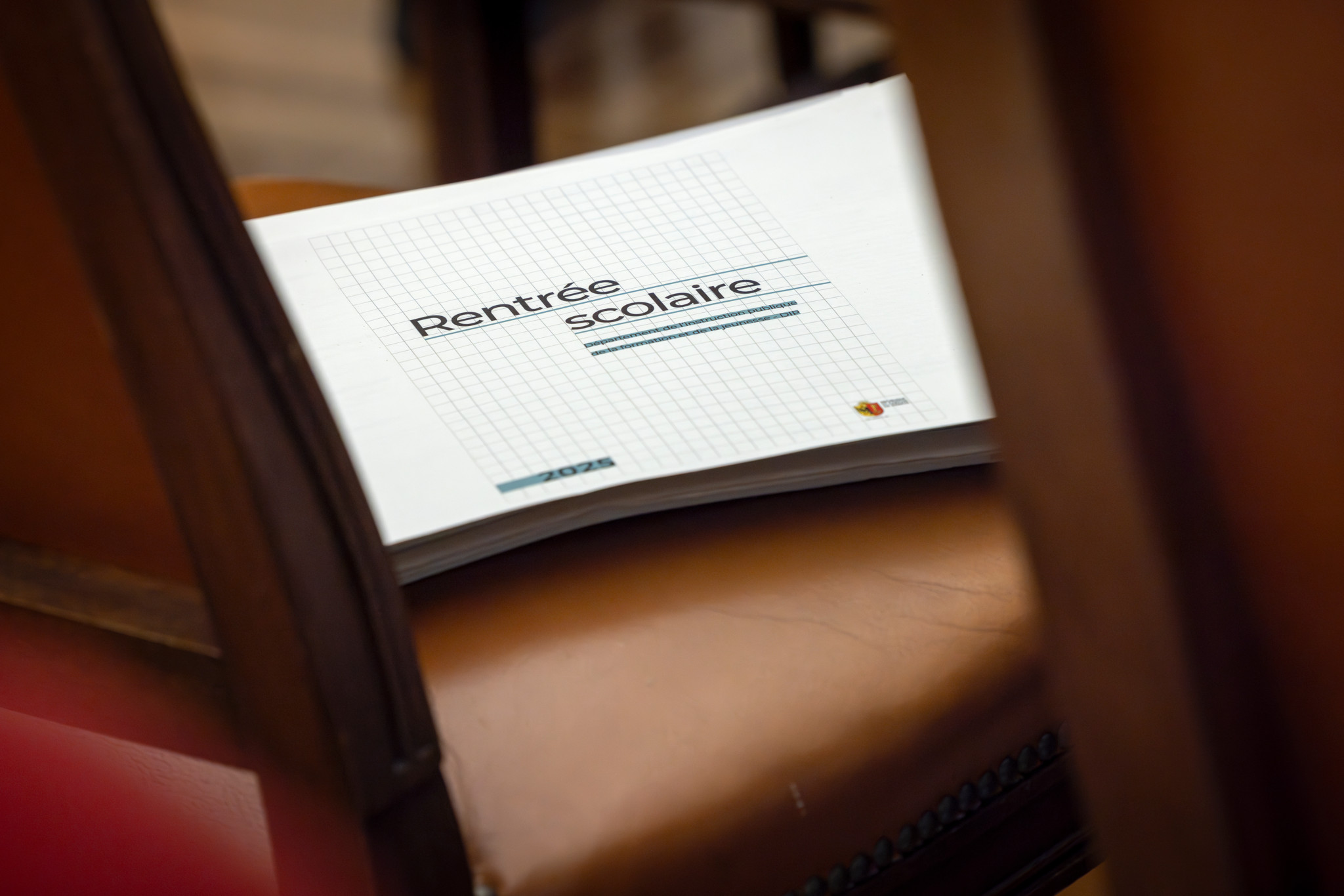 Cahier de rentrée scolaire avec texte ’Rentrée scolaire’ posé sur une chaise en bois, lors de la conférence de presse à Genève.