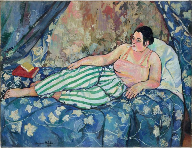 Peinture d’une femme allongée sur un canapé, portant un pantalon rayé vert et blanc, avec un livre rouge à côté d’elle.