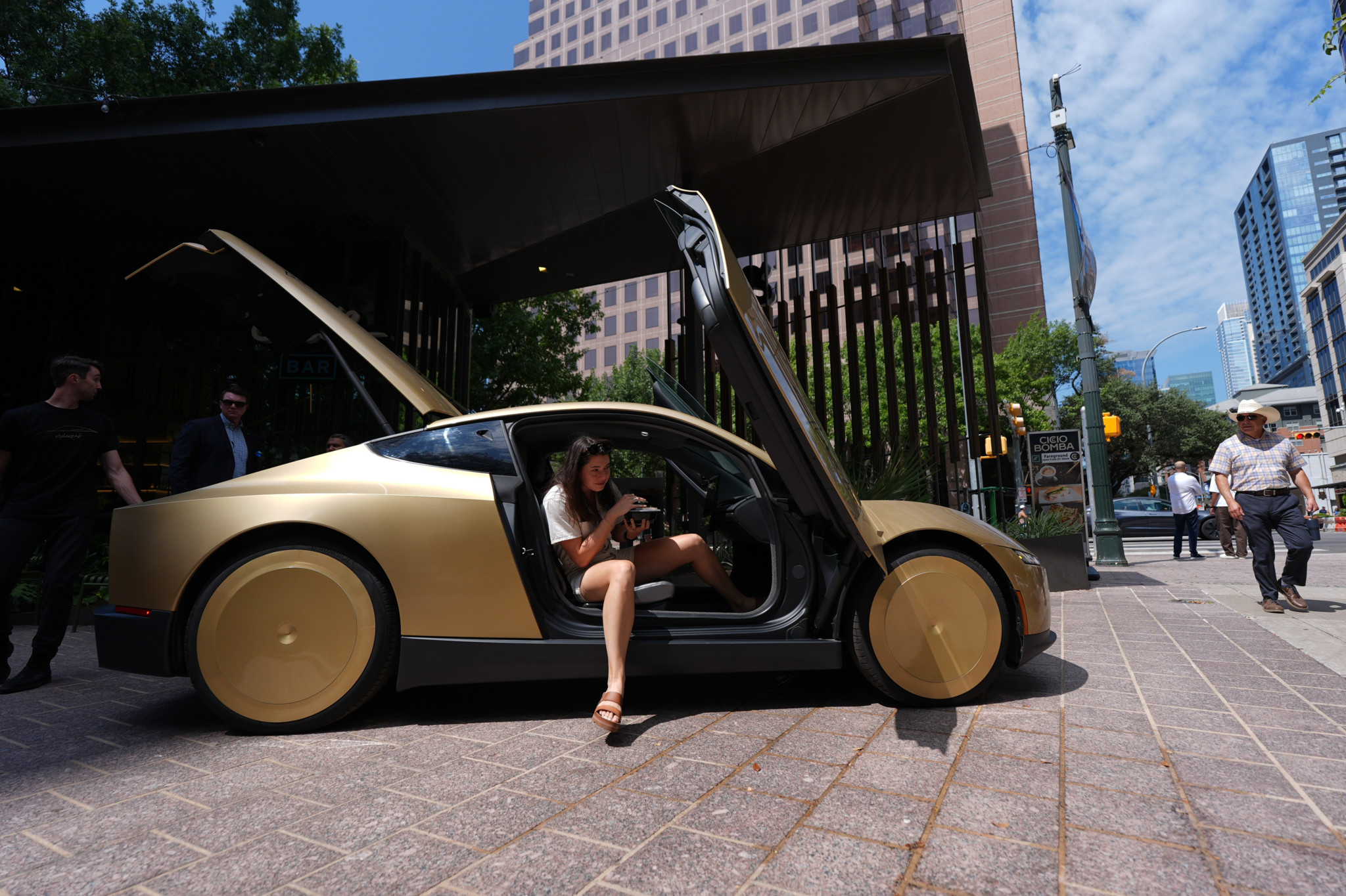 Eine Frau steigt aus einem goldenen Tesla Cybercab in der Innenstadt von Austin, Texas, mit geöffneter Flügeltür.