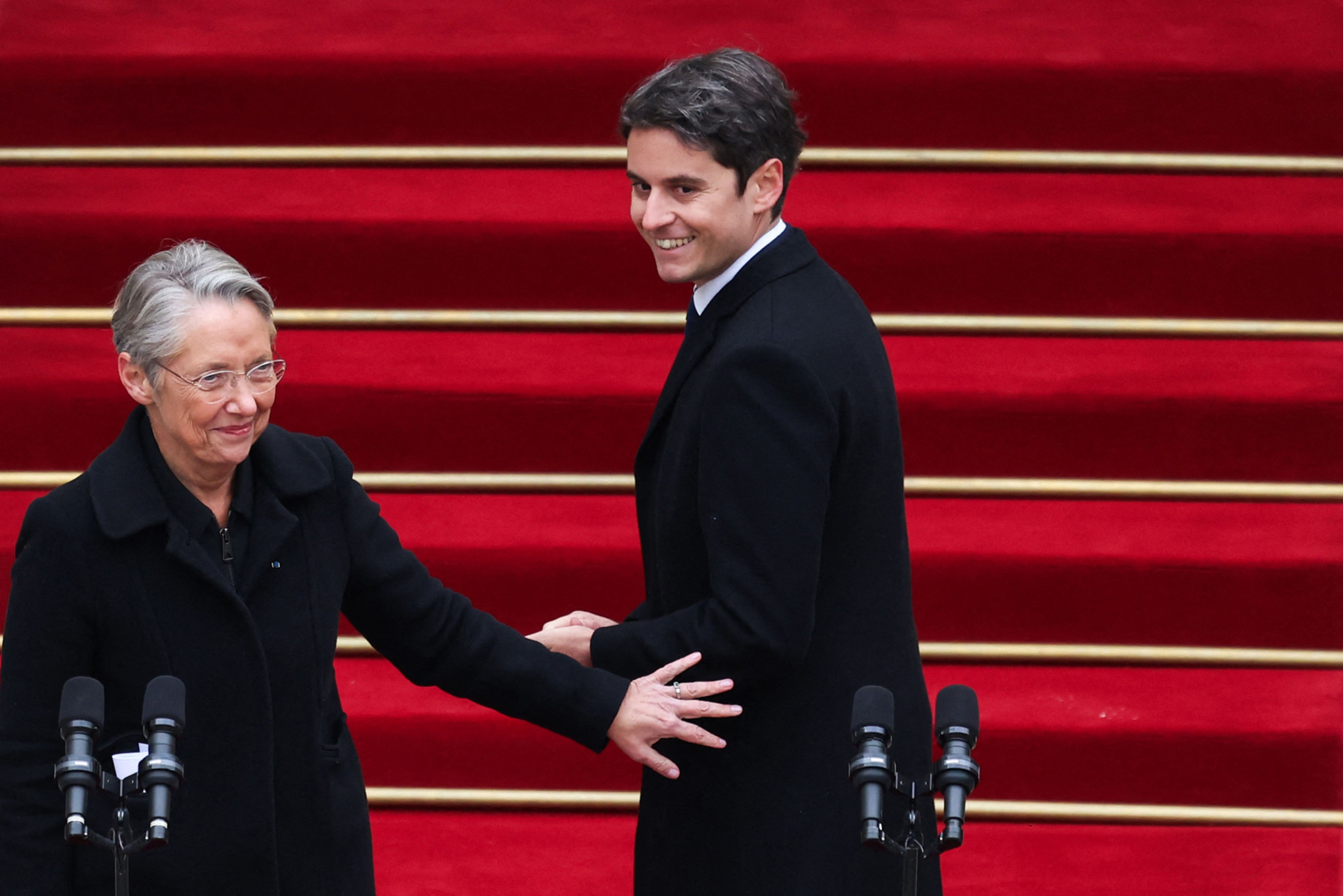 Newly appointed Prime minister Gabriel Attal (R) greets outgoing Prime minister Elisabeth Borne (L) at the end of the handover ceremony at the Hotel Matignon in Paris, on January 9, 2024. (Photo by EMMANUEL DUNAND / POOL / AFP)