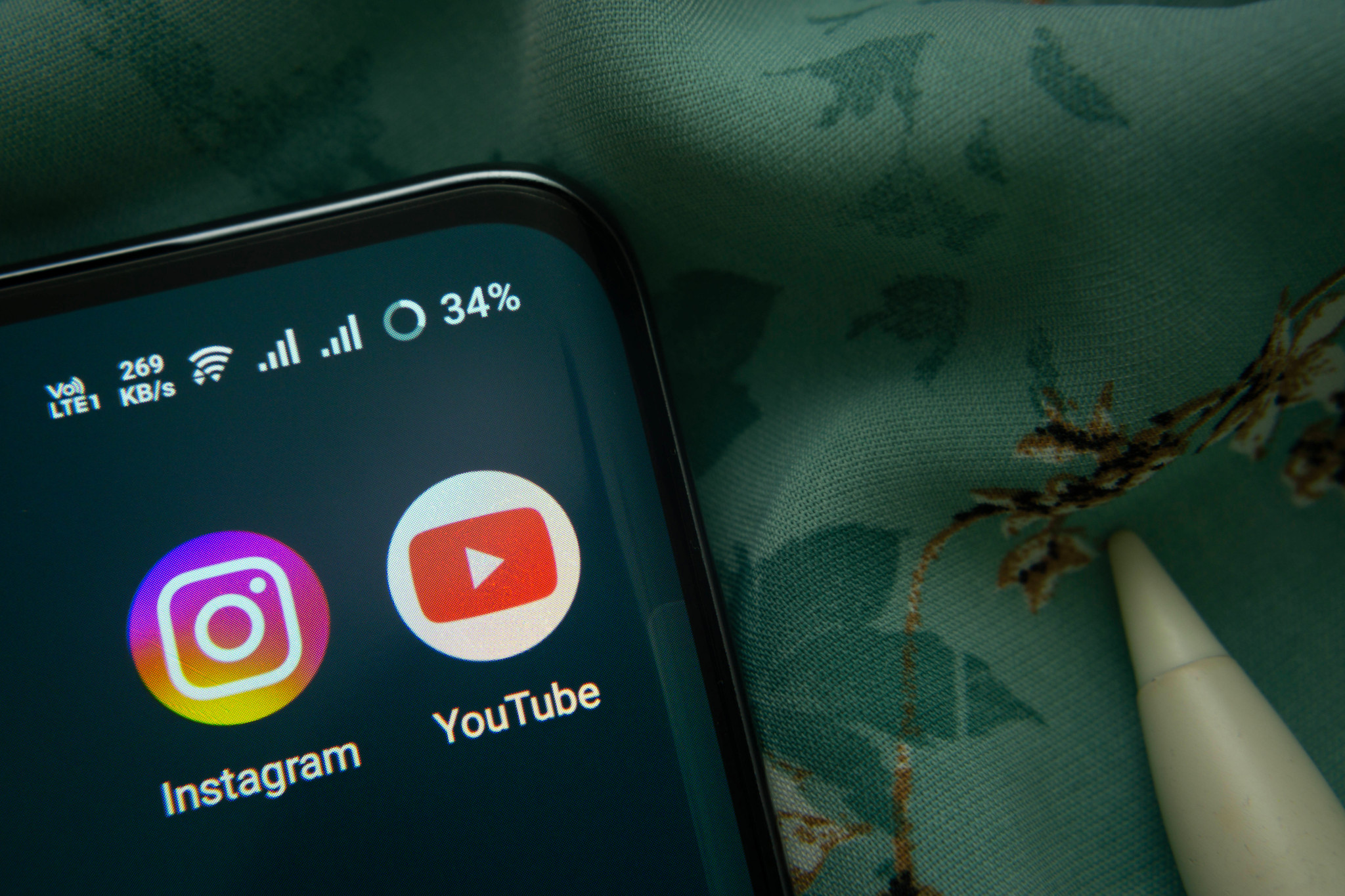 Icônes des applications Instagram et YouTube affichées sur l’écran d’un smartphone posé sur un tissu vert.