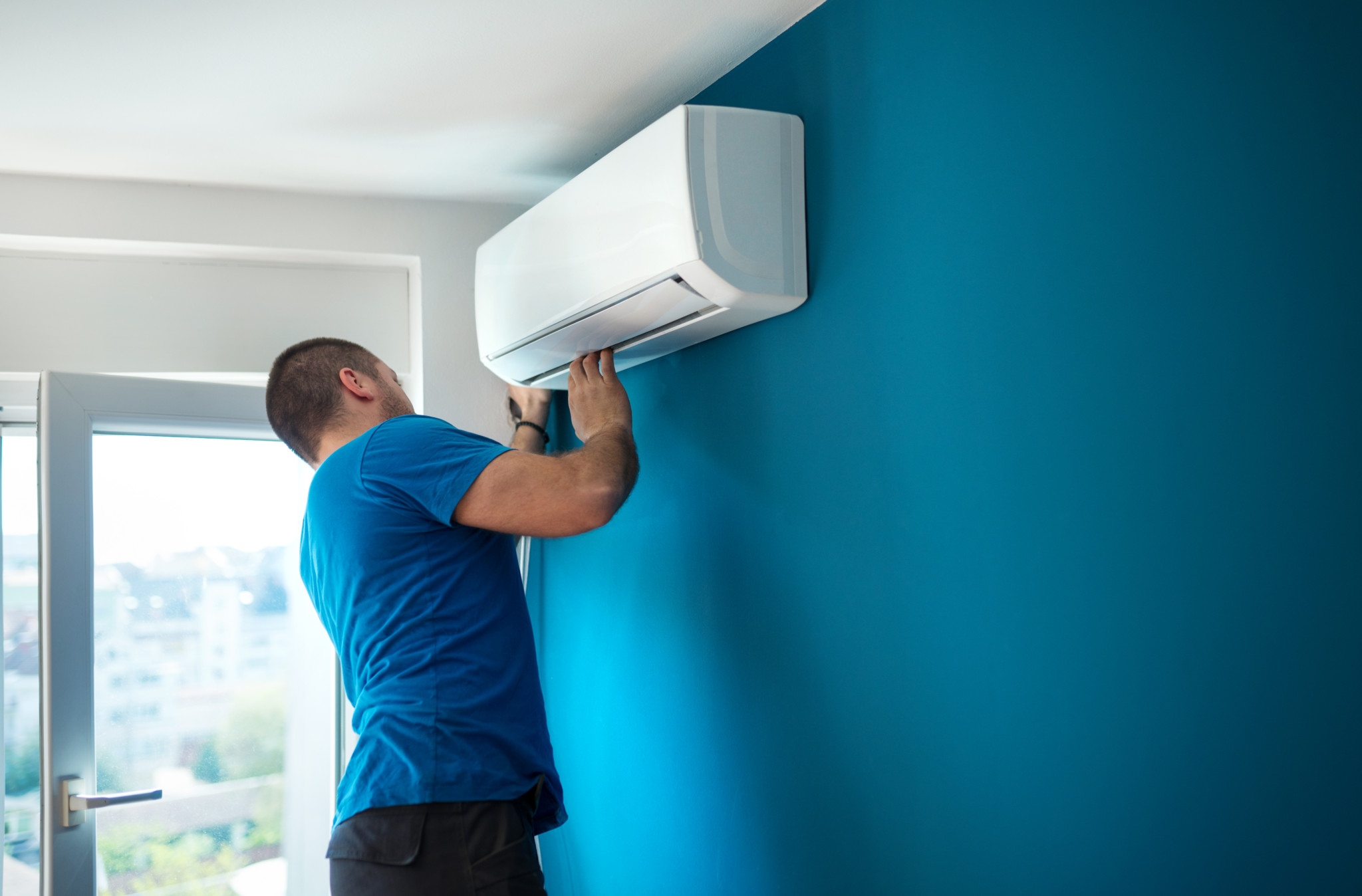 Fachmann in blauem T-Shirt installiert Inneneinheit einer Split-Klimaanlage an blauer Wand. Fachmann in blauem T-Shirt installiert Inneneinheit einer Split-Klimaanlage an blauer Wand.