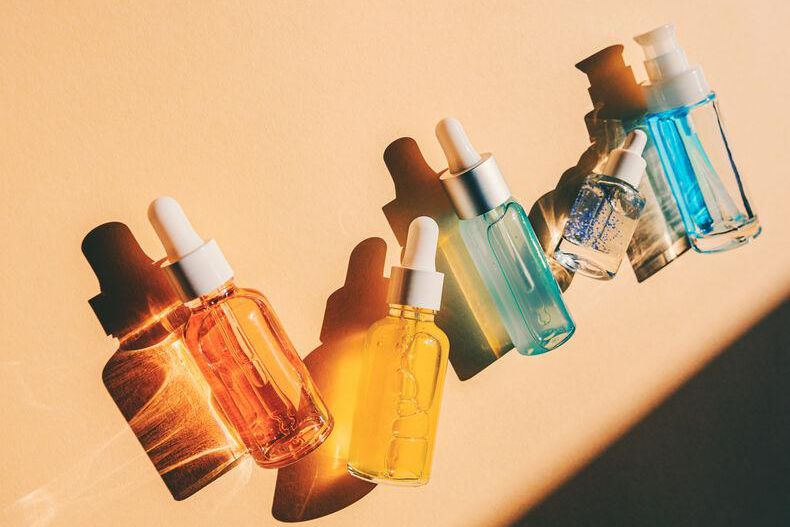 Flacons de sérums colorés illuminés par le soleil sur fond beige.