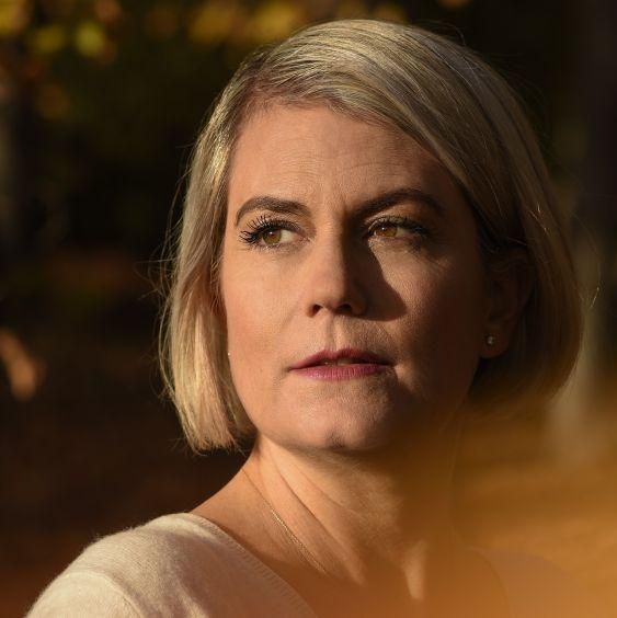 Florence Stumpe regardant au loin, éclairée par une lumière chaude et dorée, avec un fond flou de nature automnale.