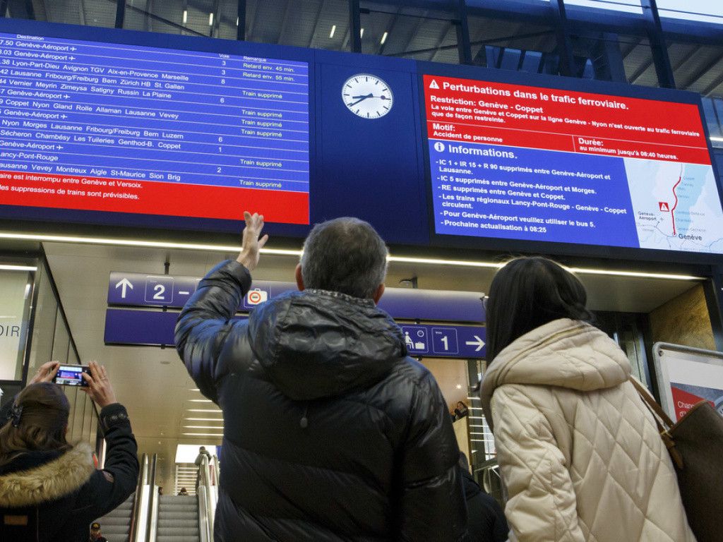 Des passagers observent le panneau des horaires de trains dans une gare.