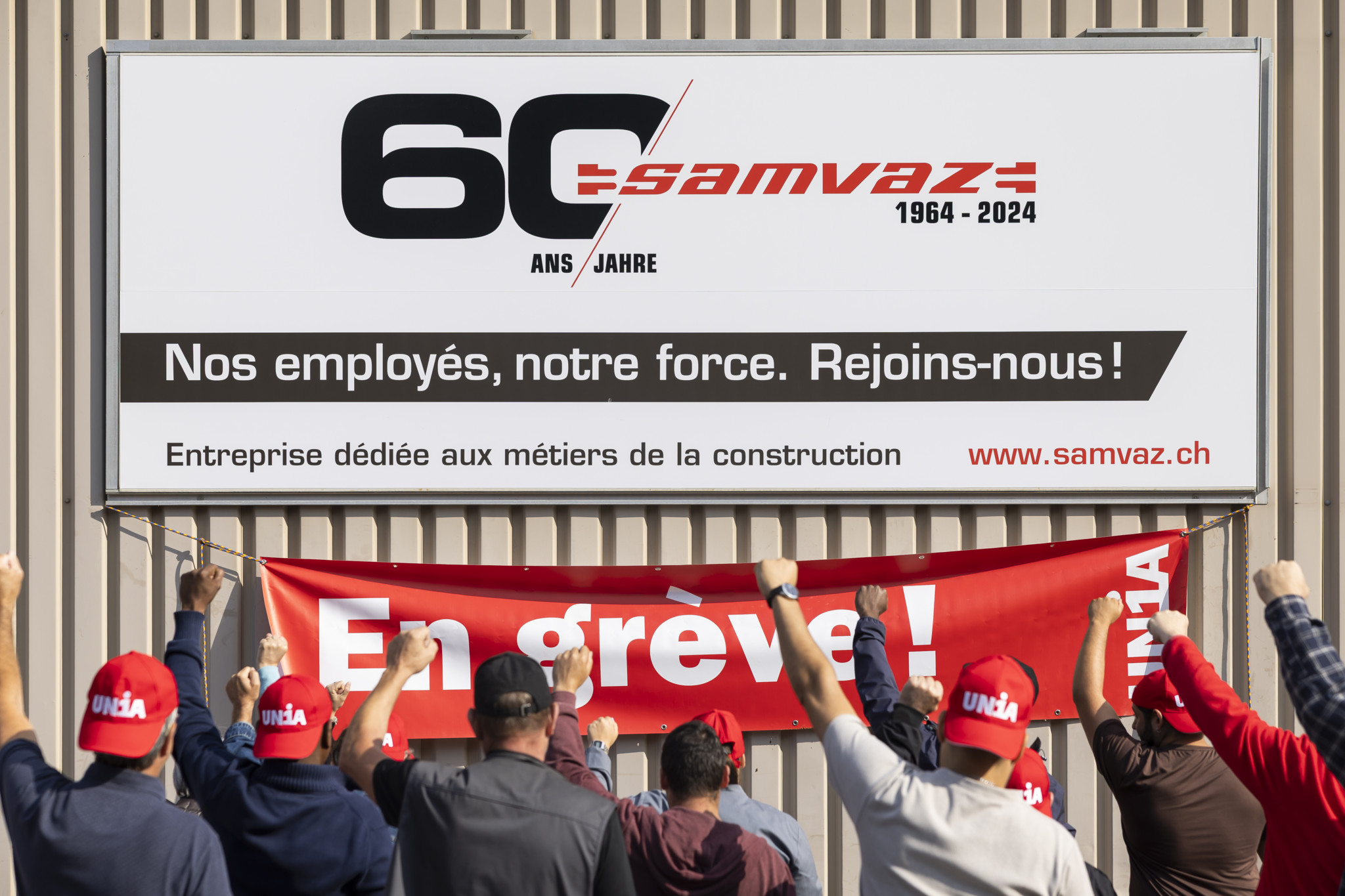 Des employés de Samvaz et membres du syndicat UNIA lèvent le poing devant une banderole ’En grève !’ à Châtel-Saint-Denis.