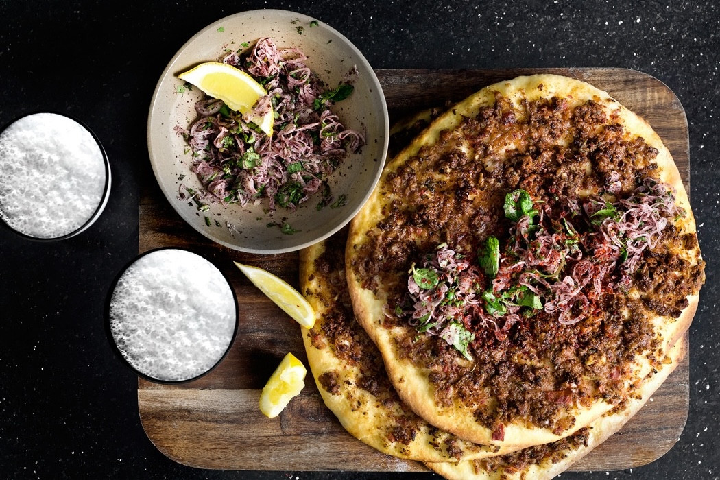 Türkische Lahmacun mit Hackfleisch und frischen Kräutern auf Holzbrett, serviert mit Salat und Zitronenspalten