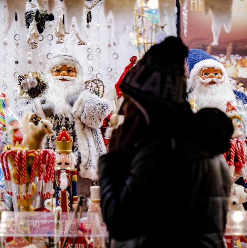 Eine Person steht vor einem weihnachtlichen Schaufenster voller bunter Süssigkeiten und Dekorationen, darunter Weihnachtsmann-Figuren.