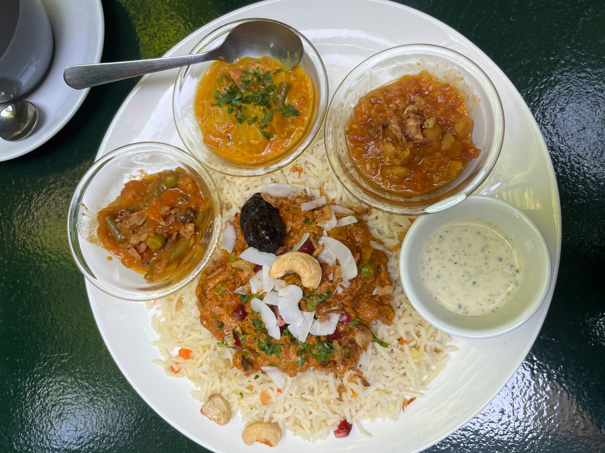 Indisches Thali mit Basmatireis, verschiedenen Currys, Cashewnüssen, Kokosraspeln und Raita auf einem weissen Teller.