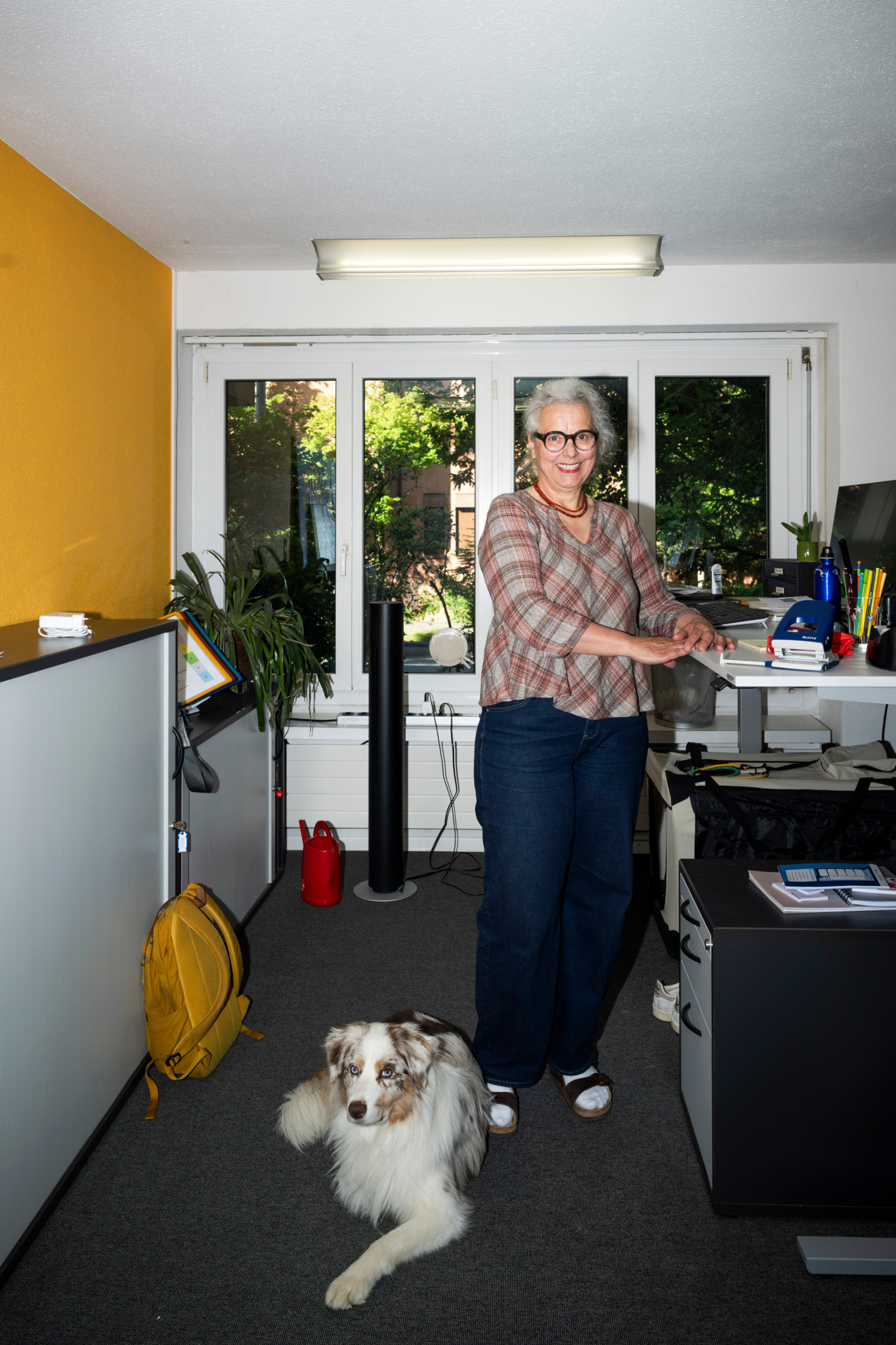 Cornelia Bärlocher, directrice du foyer Beth Chama, debout dans son bureau avec un chien border collie couché à ses pieds. Cornelia Bärlocher, directrice du foyer Beth Chama, debout dans son bureau avec un chien border collie couché à ses pieds.
