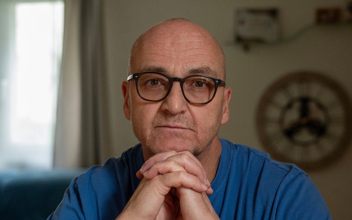 Un homme sérieux en t-shirt bleu, assis, les mains jointes devant lui, chez Serge Rufi à Romanel-sur-Lausanne, témoignage sur les commotions cérébrales.