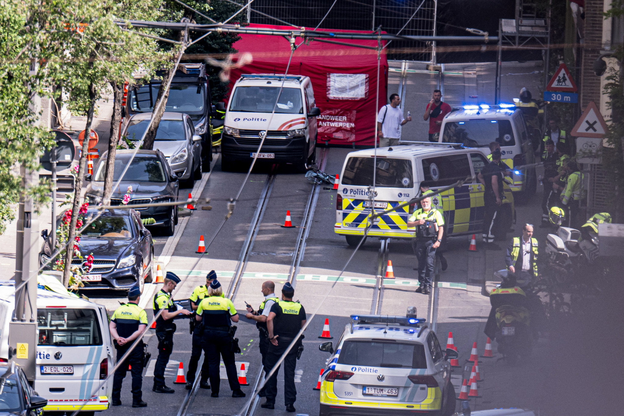 Verkehrsunfallstelle in Antwerpen mit mehreren Polizisten, die den Ort sichern, wo ein Polizeifahrzeug angeblich einen 9-jährigen Jungen erfasst hat. Mehrere Polizeifahrzeuge und ein Rettungszelt sind sichtbar.