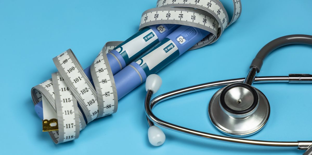 Ozempic Insulin-Injektionspen umwickelt mit einem Massband neben einem Stethoskop auf blauem Hintergrund