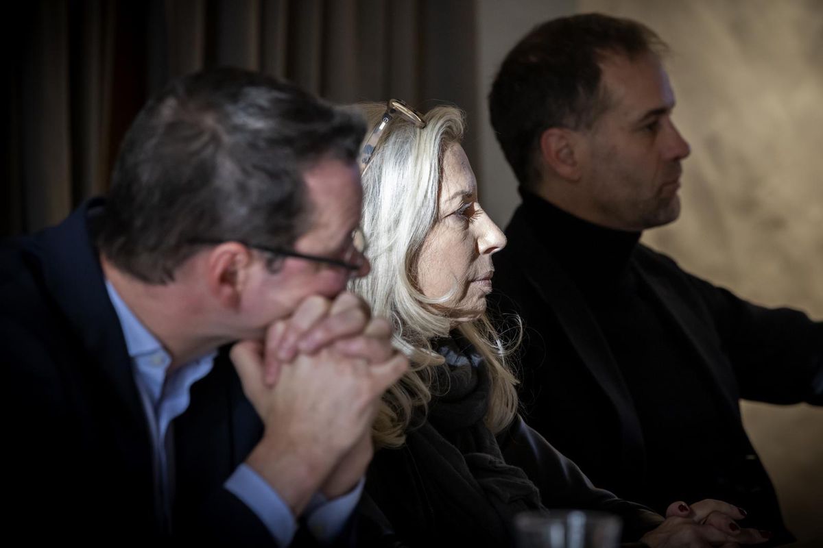 Trois personnes assises à une réunion, concentrées, vêtues de vêtements formels.