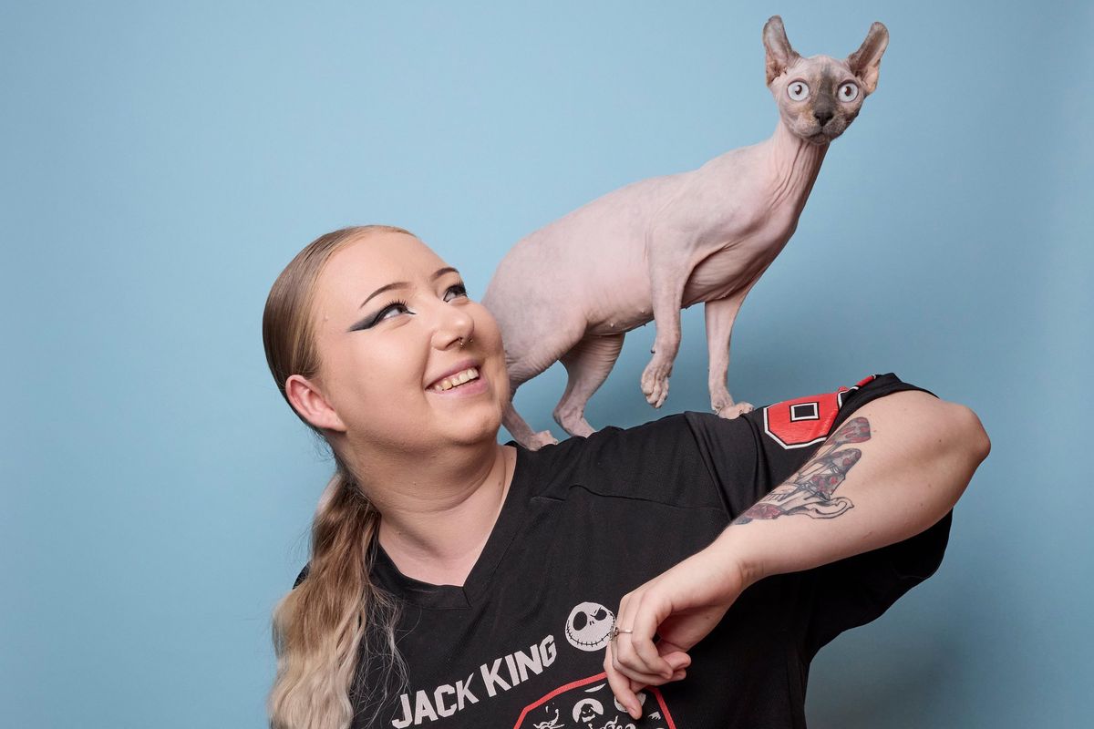 Une femme souriante avec un chat sphinx sur l’épaule, posant contre un fond bleu à La Tour-de-Peilz.