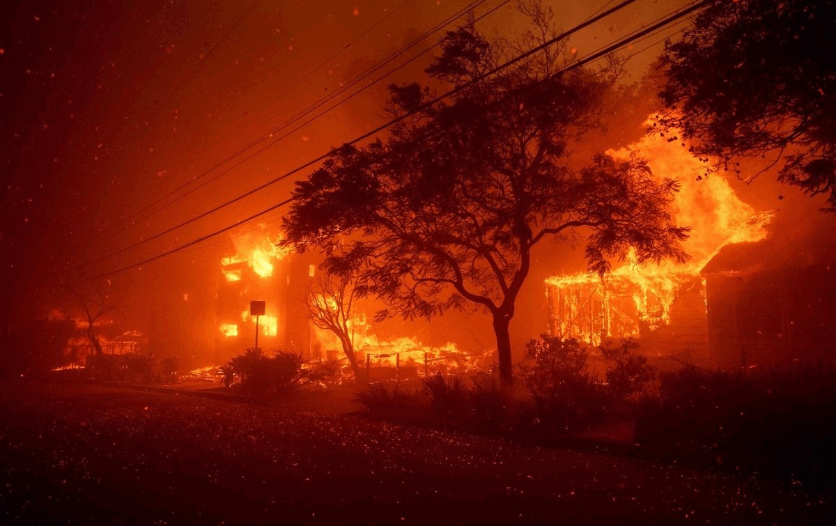 Ein intensives Feuer erhellt die Nacht, Bäume und Gebäude stehen in Flammen. Die Szene ist von Rauch und Funken durchsetzt.