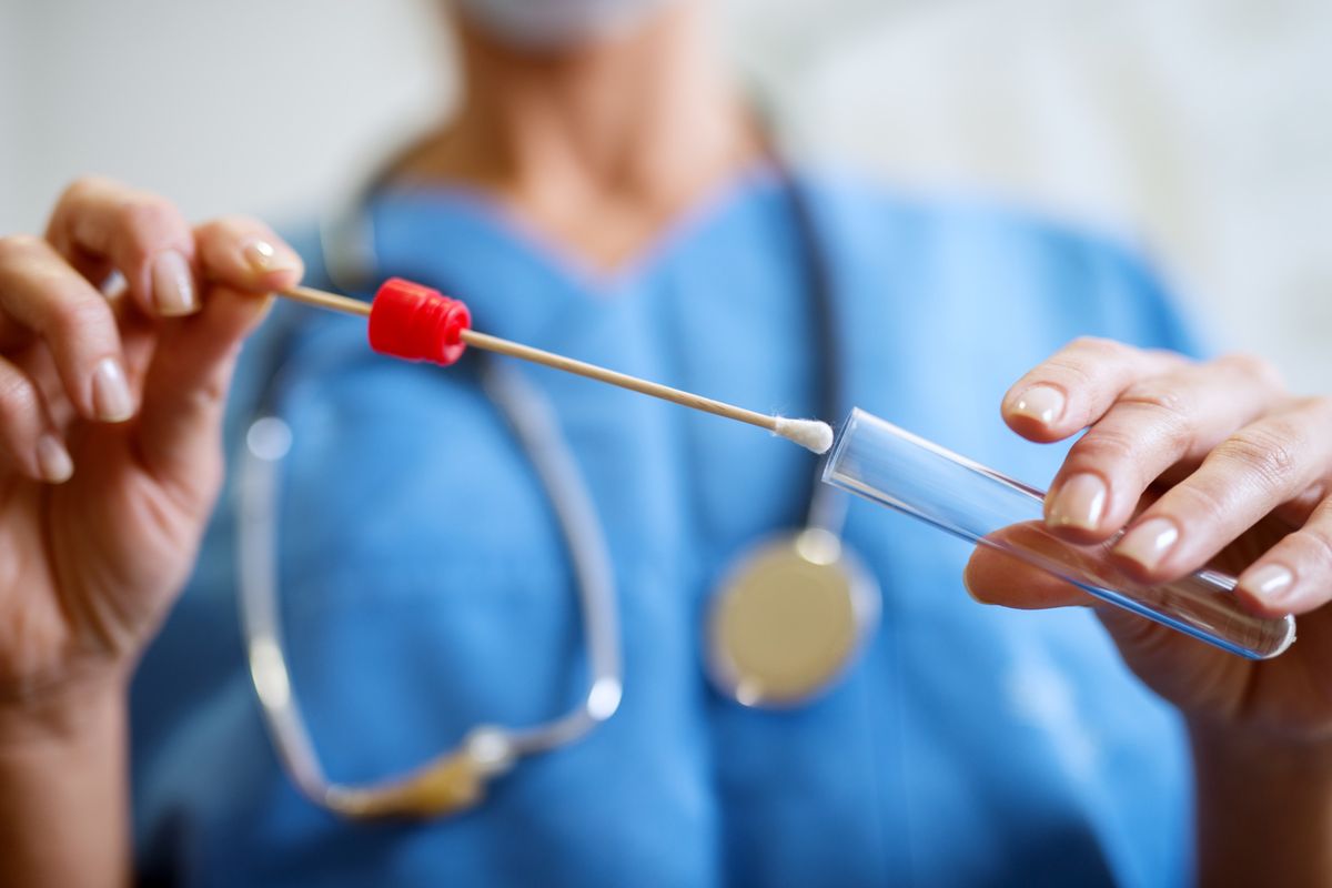 Close up of nurses hands holding buccal cotton swab and test tube ready to collect DNA from the cells.
