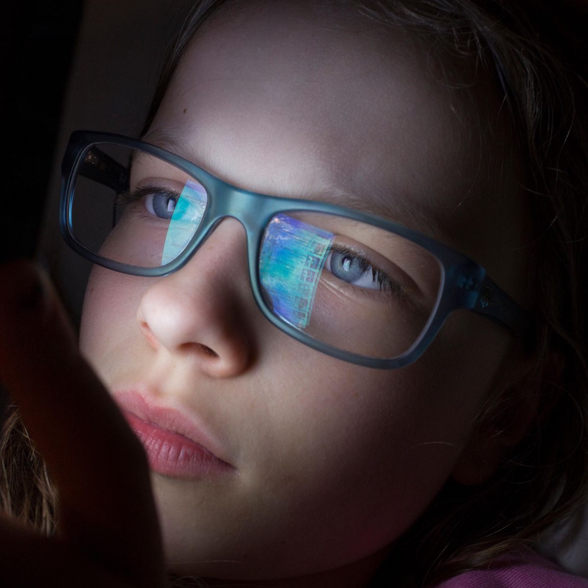 Jeune fille portant des lunettes, utilisant un smartphone, avec la lumière de l’écran réfléchie sur ses verres.