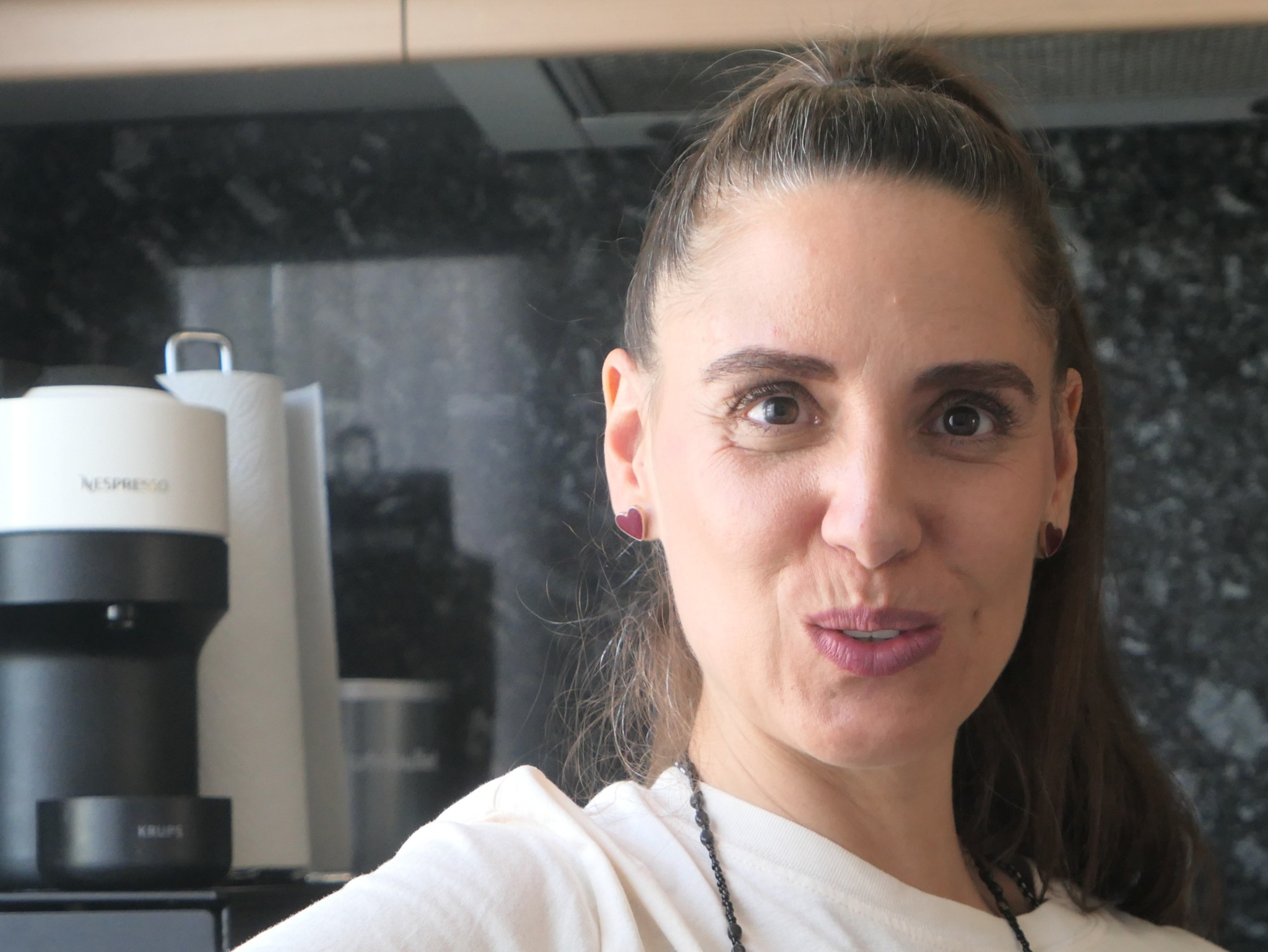 Frau mit hochgebundenem Haar in einer Küche, im Hintergrund eine Nespresso-Kaffeemaschine auf der Arbeitsfläche.