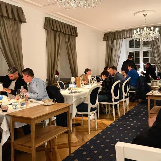 Elegantes Restaurant mit Kronleuchtern, Gästen an weiss gedeckten Tischen sitzend, in gedämpftem Licht speisend.