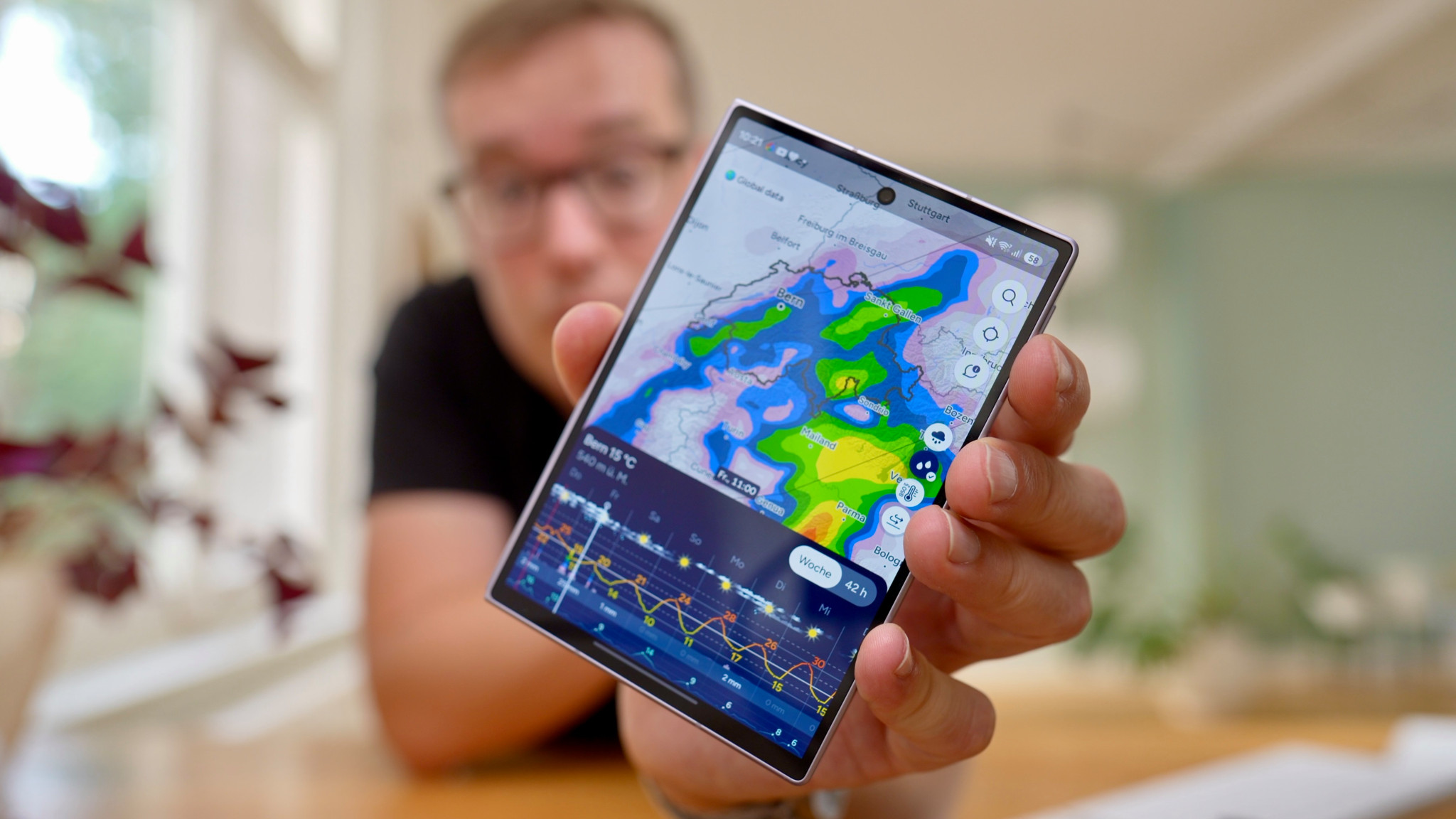 Rafael Zeier hält Smartphone mit farbiger Wetterkarte und Regenradar der App Fluid in die Kamera
