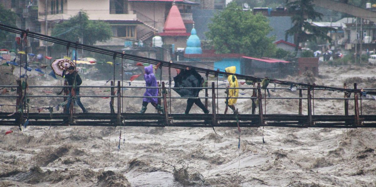 Des personnes traversent un pont sous la pluie à Kullu District, en Inde.