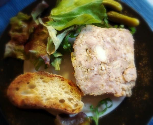 Plat de terrine de viande avec des toasts, des cornichons et une salade sur une assiette.