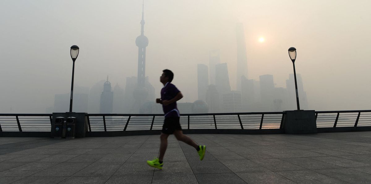 Un joggeur court sur une promenade au bord de l'eau avec la skyline d'une ville brumeuse en arrière-plan.