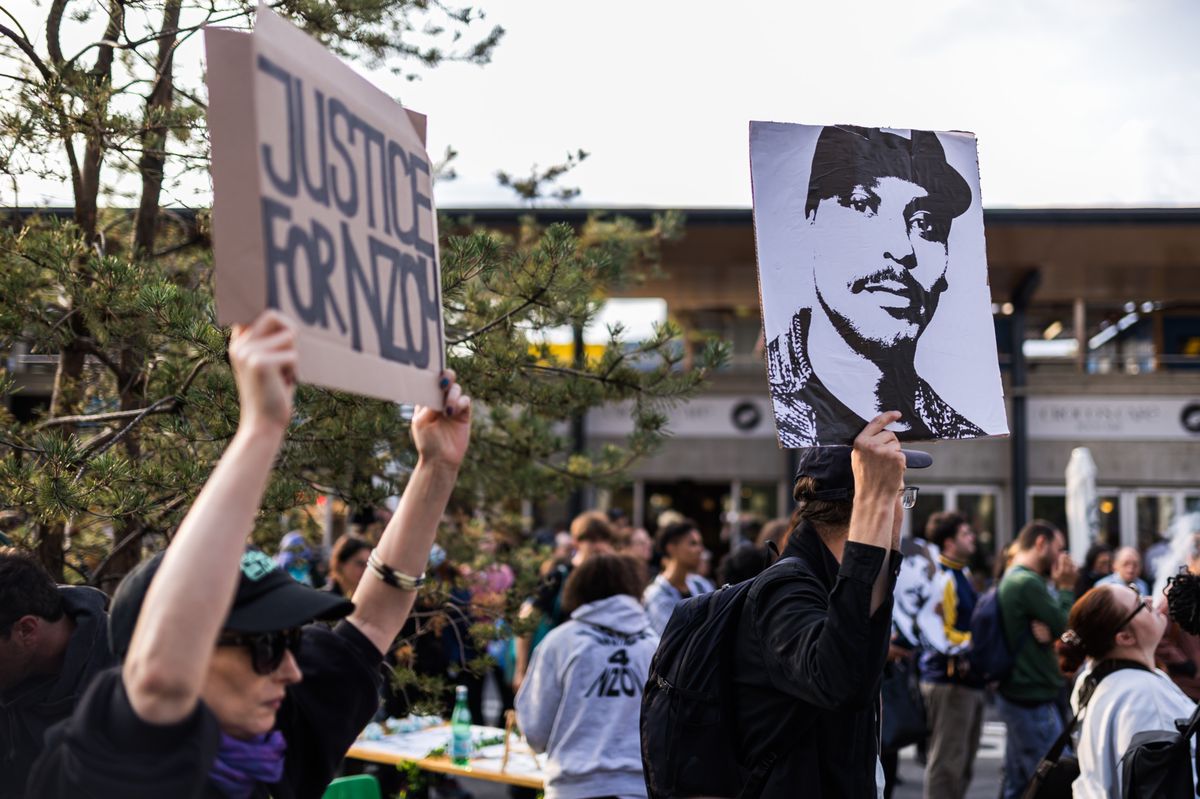 Une personne tient une banderole " justice pour Nzoy " et une autre personne tient le portrait de Nzoy lors d'un rassemblement devant l'entree de la gare CFF de Morges a la memoire de Nzoy, tue par balle par un policier, ce mercredi 30 aout 2023 a Morges. Une centaine de personnes se sont rassemblees mercredi soir a la gare de Morges a la memoire d'un homme tue par balle par un policier le 30 aout 2021.  (KEYSTONE/Pierre Albouy)