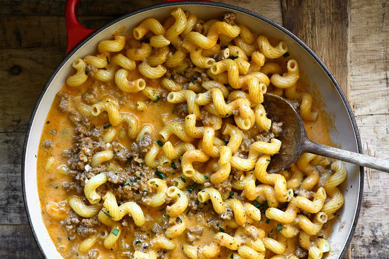 Cremige Cavatappi-Nudeln mit Hackfleisch in einer roten Pfanne, serviert mit einem Holzlöffel.